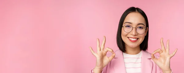 Etkilenmiş kurumsal kadının yakın portresi, gözlüklü Asyalı iş kadını, tamam işareti gösteren, kameraya hayran bakan, tavsiye eden, pembe arka plan — Stok fotoğraf