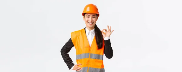 Architecte asiatique professionnelle confiante dans casque de sécurité assurer la qualité et le travail dans le temps, montrant un geste correct et souriant déterminé, debout affirmatif, assurer et garantir quelque chose — Photo