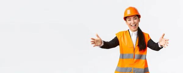 Přátelsky usměvavá asijská stavební manažerka, inženýrka v bezpečnostní přilbě a reflexní bundě, natažené ruce pro pozdrav, vítaní obchodních partnerů, stojící na bílém pozadí — Stock fotografie