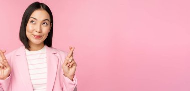 Mutlu iş kadını, Asyalı kurumsal bayan diliyor, diliyor, diliyor, dua ediyor, pembe arka planda takım elbise içinde duruyor.