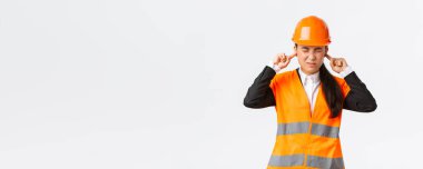 Asyalı bayan şirket yöneticisi rahatsız hissediyor, baş mühendis kulaklarını kapatıyor ve sinir bozucu gürültüden yüzünü buruşturuyor, inşaat alanındaki işleri denetliyor, korkunç bir tamir sesi, güvenlik kaskı takıyor.