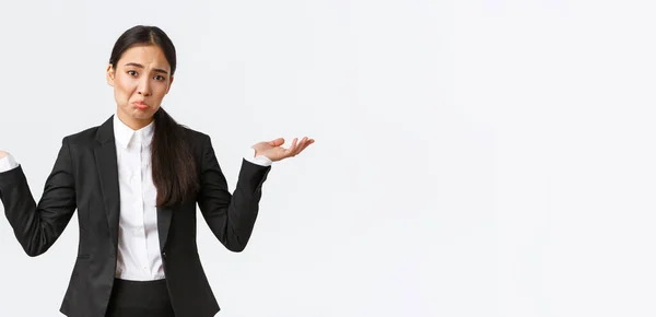 Clueless upset young asian female office worker, manager in black suit, shrugging with hands spread sideways and pouting unaware, dont know, cant understand, standing useless and indecisive — Stock Photo, Image