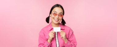 Şık, modern Asyalı kız portresi, indirim, kredi kartı ve memnun görünme, temassız ödeme, alışveriş konsepti, pembe arka planda dikilme