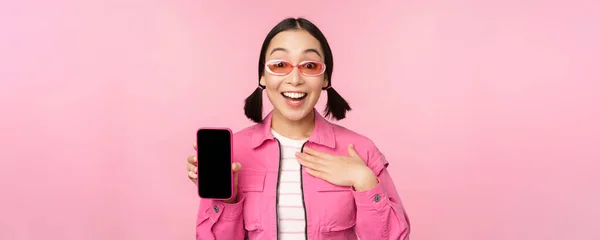 Obraz zaskoczonej dziewczyny wyświetlającej ekran aplikacji telefonu komórkowego, wyświetlacz smartfona, interfejs aplikacji, stojącej na różowym tle — Zdjęcie stockowe