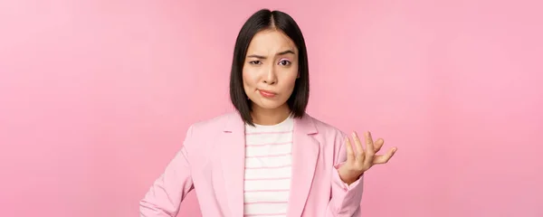 怒っているアジアの女性の肖像画でスーツ、松葉杖拳と見て激怒し、笑顔悪いの激怒、ピンクの背景の上に立って — ストック写真
