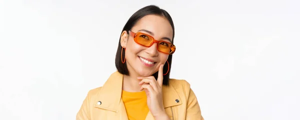 Primer plano retrato de mujer asiática pensando, usando gafas de sol y sonriendo, mirando hacia arriba reflexivo, de pie sobre fondo blanco estudio — Foto de Stock