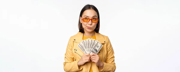 Microcredit and money concept. Stylish asian young woman in sunglasses, laughing happy, holding dollars cash, standing over white background — Stock Photo, Image