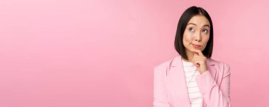 Asyalı iş kadınının düşünceli duruşu, beyin geliştirmesi, takım elbise giymesi. Koreli satıcı, pembe arka planda poz veren girişimci.