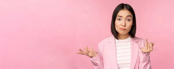 아시아 사업가인 젊은 여성의 모습, 판매원인 여성 이 어깨를 으쓱 하고 핑크 색 배경 위에 서 있는 혼란스럽고 무색 해 보이는 모습 — 스톡 사진