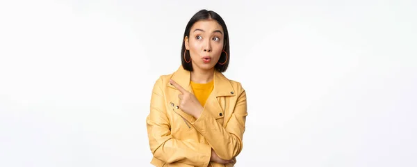 Afbeelding van een verbaasde vrouw met de vinger naar links, naar het logo of de banier kijkend met een geïntrigeerde gezichtsuitdrukking, staande over een witte achtergrond — Stockfoto