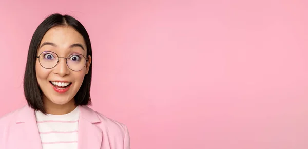 Крупним планом портрет азіатської бізнес-леді в окулярах дивиться здивовано на камеру, вражений реакцією, що стоїть в костюмі над рожевим тлом — стокове фото