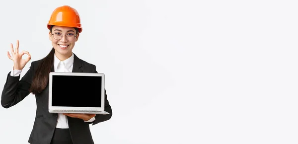 프로페셔널 여성 건축가, 공장의 건설 매니저, 그래프, 긍정도 다이어그램, 승인에 좋은 제스처를 만들고 스크린을 향하는 노트북을 들고 안전 헬멧을 착용하고 — 스톡 사진