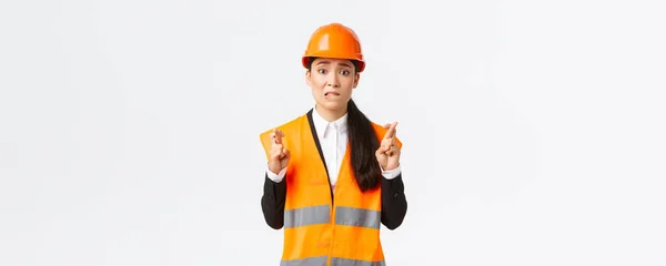 Preocupado esperançoso asiático arquiteto feminino sentindo nervoso como esperando por resultados de inspeção na área de construção, vestindo capacete de segurança, dedos cruzados boa sorte, espero que tudo esteja bem — Fotografia de Stock