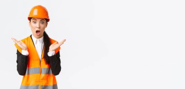 Yansıtıcı ceketli, güvenlik kasklı Asyalı kadın mühendis, beklenmedik haberlere tepki veriyor, ellerini kaldırıyor ve alkışlıyor, inşaat alanını ziyaret ediyor, harika bir iş çıkarmaktan memnun.