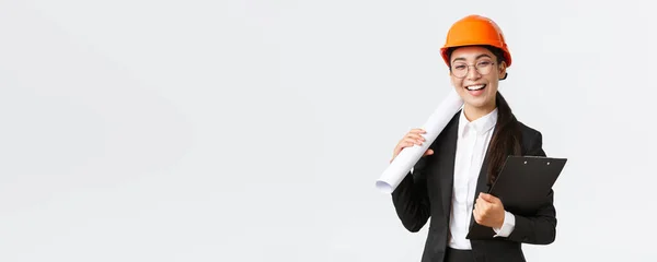 Profesional feliz asiática arquitecta, ingeniero de construcción en casco y traje de negocios con planos y portapapeles con documentación de construcción, sonriente alegre, fondo blanco — Foto de Stock