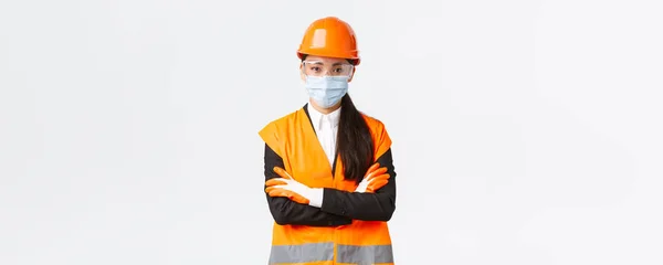 Girişim, inşaat ve virüs konseptini önleme konusunda Covid-19 güvenlik protokolü. Koronavirüs sırasında işçilerin protokole uyup, maske takmadıklarına bakan kendinden emin Asyalı kadın başmühendis. — Stok fotoğraf