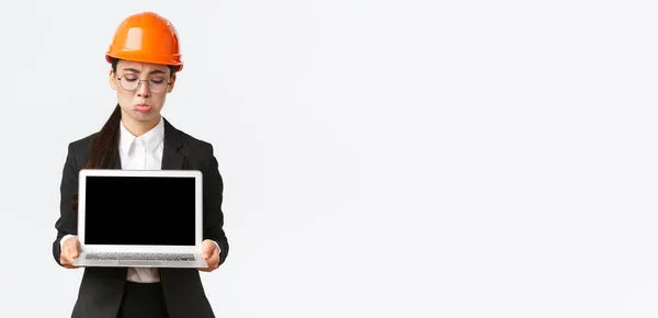 안전 헬멧과 비지니스 수트를 착용하고 노트북 컴퓨터를 들고 스크린을 보며 실망 한 실망 한 나머지 백그라운드 토픽을 하며 서 있는 여성 기술자 — 스톡 사진
