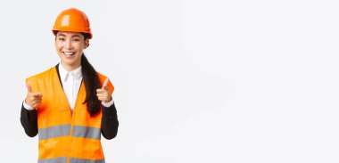 Güvenlik kaskı ve yansıtıcı ceketli, kendine güvenen Asyalı kadın inşaat yöneticisi, kamerayı işaret ederek iyi seçim, iyi iş ya da iyi iş, beyaz arka plan,