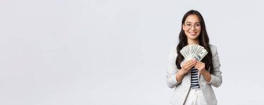 İş, finans ve istihdam, girişimci ve para kavramı. Başarılı genç Asyalı ofis müdürü, para kazanan bir iş kadını, elinde dolar tutuyormuş gibi gülümsüyor.