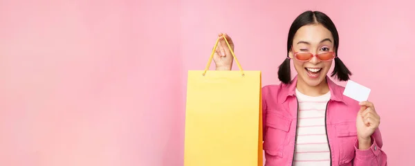 快乐的年轻亚洲女人带着信用卡购物、提包、购物、购物、购物、购物、站在粉色背景上 — 图库照片