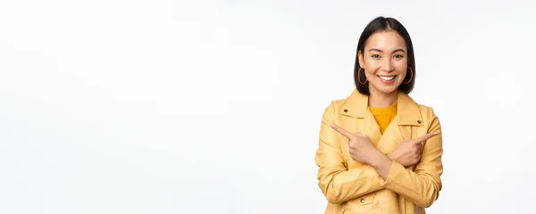 Image d'une fille asiatique indécise, pointant du doigt latéralement, pointant à gauche et à droite, choisissant une variante, décidant, debout sur fond blanc — Photo