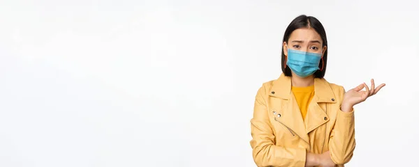 Mujer asiática confusa en máscara facial médica, buscando despistado, perplejo, usando máscara facial médica, de pie sobre fondo de estudio blanco — Foto de Stock