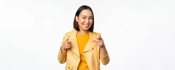 Ehi, tu. Felice sorridente donna asiatica puntando il dito contro la macchina fotografica, scegliendo, congratulandosi e lodando voi, in piedi su sfondo bianco — Foto Stock