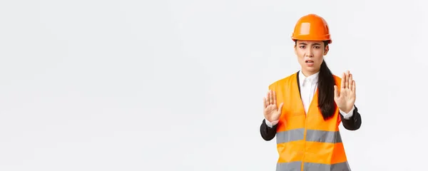 Teleurgesteld boze Aziatische vrouwelijke ingenieur in veiligheidshelm en reflecterende kleding te zeggen stop, verbieden en oneens met de bouw manager, tonen genoeg, geen gebaar, witte achtergrond — Stockfoto