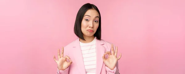 Niet slecht. Indrukwekkende zakenvrouw, aziatische kantoor dame tonen oke teken en knikken in goedkeuring, staande over roze achtergrond — Stockfoto