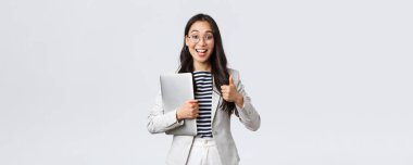 İş, finans ve istihdam, başarılı kadın girişimciler konsepti. Gözlüklü genç kendine güvenen iş kadını, baş parmak işareti yapıyor, dizüstü bilgisayarı tutuyor, en iyi hizmet kalitesini garanti ediyor.