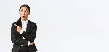 Etkileyici Asyalı bayan menajer, takım elbiseli iş kadını sol üst köşeyi işaret ediyor ve bakıyor.