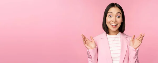 Retrato de una mujer de negocios asiática mirando sorprendida a la cámara, aplaudiendo y mirando emocionada, sonriendo, posando sobre fondo rosa —  Fotos de Stock