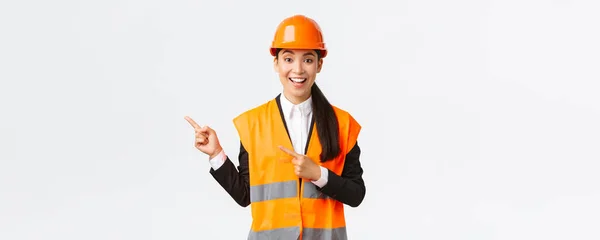 Будівництво, будівництво та промислова концепція. Усміхнена жінка-інженер в шоломі та одязі, що відображає спосіб, вказуючи верхній лівий кут, говорячи про будівництво проекту, білий фон — стокове фото
