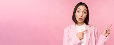 Hevesli profesyonel iş kadını, tezgahtar kadın parmaklarını sağa göstererek reklam ya da şirket logosunu bir kenara bırakıp pembe arka planda poz veriyor.