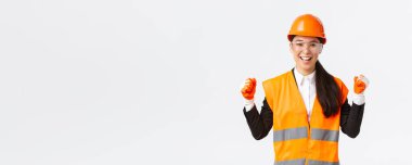 Başarılı Asyalı kadın mühendis, koruyucu gözlüklü inşaat mimarı, eldiven ve kask zaferi, yumruk pompası sevinci ve evet, hedefe ulaş, beyaz arka plan