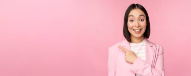 Asyalı iş kadını portresi, takım elbiseli kadın sol eli, pankart reklamını gösteriyor, gülümsüyor ve profesyonel görünüyor, pembe arka plan