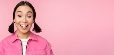 Güzel Asyalı kızın portresini yakından çek. Hevesli ve gülümseyen, gülümseyen, pembe arka planda mutlu duran.