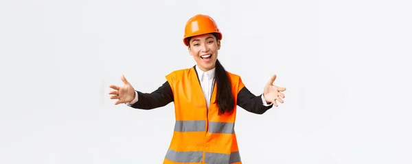 Amigável sorrindo asiático feminino gerente de construção, engenheiro em capacete de segurança e jaqueta reflexiva, estendendo as mãos para saudação, bem-vindo parceiros de negócios, de pé fundo branco — Fotografia de Stock