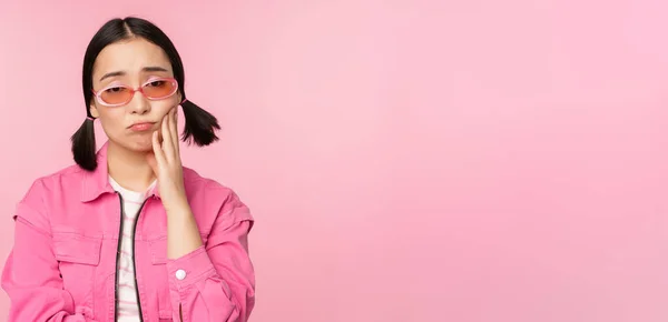 Immagine di triste ragazza asiatica imbronciato, toccando la guancia, il broncio deluso, ha mal di denti, in piedi su sfondo rosa — Foto Stock