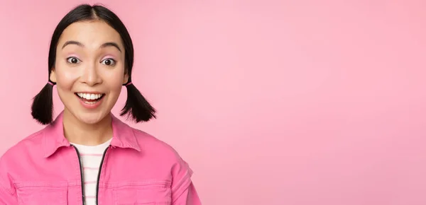 Close-up portret van mooi aziatisch meisje op zoek enthousiast en glimlachend, lachen en glimlachen, staande gelukkig tegen roze achtergrond — Stockfoto