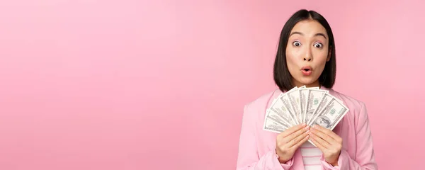 Finance, microcredit and people concept. Happy smiling asian businesswoman showing dollars money, standing in suit against pink background — Stock Photo, Image