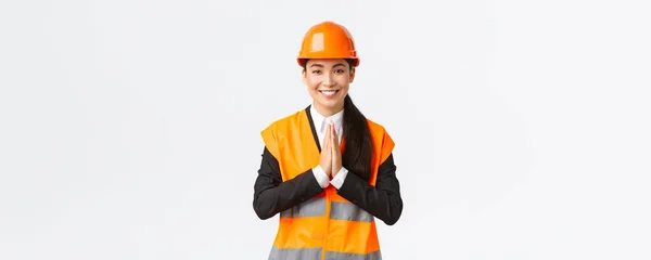 Улыбающиеся благодарные азиатские женщины-архитектор воспринимают веру клиентов, держатся за руки в мольбе, благодарят кого-то, носят защитный шлем и пиджак, стоя на белом фоне ценят все — стоковое фото
