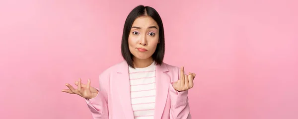 Portrait de jeune femme d'affaires asiatique, vendeuse haussant les épaules et regardant confus, sans aucune idée de smth, debout sur fond rose — Photo