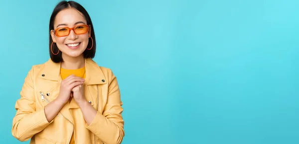 Portrait de femme asiatique en lunettes de soleil, regardant plein d'espoir, flatté, souriant heureux, debout sur fond bleu — Photo