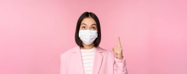 İş kadını portresi, ofis elbisesi ve tıbbi yüz maskesi takan Asyalı kadın, şirket logosunu ya da afişini gösteren, pembe arka plan.