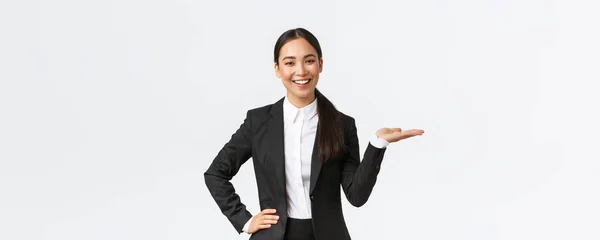 Επαγγελματική χαμογελαστή επιχειρηματίας παρουσιάζει το έργο της κατά τη διάρκεια της συνάντησης. Πωλητής με μαύρο κοστούμι κρατώντας το χέρι ως δείχνει το προϊόν, κρατώντας στην παλάμη πάνω από λευκό φόντο — Φωτογραφία Αρχείου