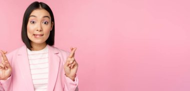 Mutlu iş kadını, Asyalı kurumsal bayan diliyor, diliyor, diliyor, dua ediyor, pembe arka planda takım elbise içinde duruyor.