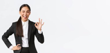 İddialı ve kendinden emin Asyalı genç iş kadını kontrol altına alındı, göz kırp ve anlaşmayı teşvik etmek için iyi bir hareket göster, iyi iş, iyi iş ya da onay jesti, mutlu ayakta durmak