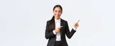 Kendine güvenen Asyalı kadın girişimci, takım elbiseli satıcı ürünleri tanıtıp müşterilere yer gösteriyor. İş kadını gülümsüyor ve parmakla pankartı işaret ediyor, beyaz arka planda duruyor.