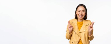 Heyecanlı Asyalı kadın portresi umut dolu, dua eden, yalvaran, haber bekleyen, beyaz arka planda duran, mutlu gülümseyen,